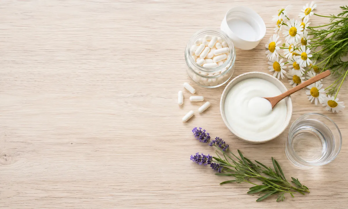 Remedios caseros para infección vaginal: cápsulas de probióticos, yogur natural, manzanilla, lavanda y agua sobre superficie de madera clara