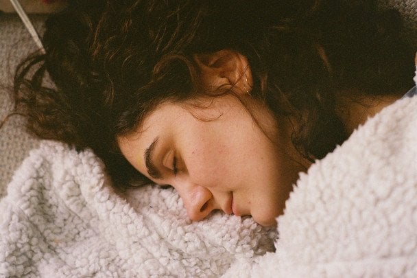 persona durmiendo de lado mostrando su postura al dormir sobre una cama con almohada blanca