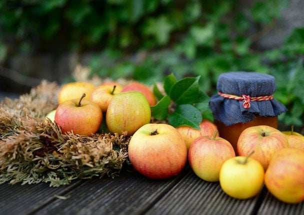 Frasco de mermelada de manzana casera junto a manzanas frescas sobre mesa de madera